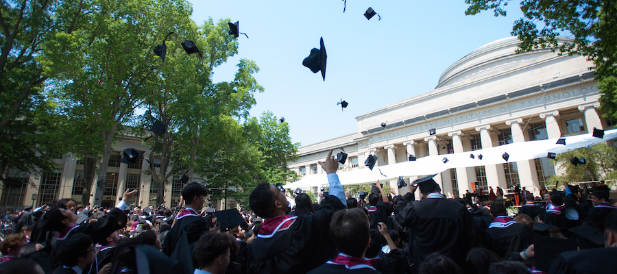 Image of graduates throwing their caps into the air. The Killian Court stage and the Lobby 10 dome can be seen in the background.