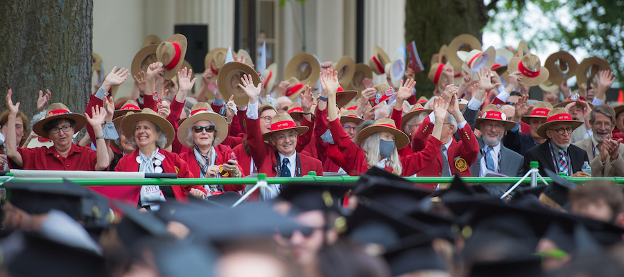 Image of alumni in their red jackets waving at the graduates