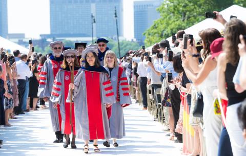 Image of the academic procession making it's way down the center aisle in Killian Court. Lily Tsai is leading the procession, holding the ceremonial shephard's crook