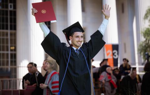 Image of graduate walking down the stage ramp after receiving his degree. He is smiling as he poses for the camera. Both of his arms are raised in excitement.