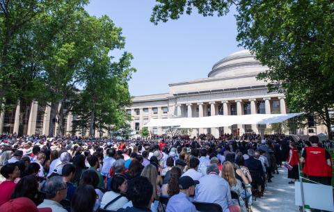Image of the audience looking towards the stage and Lobby 10 on Killian Court. The sky is blue.