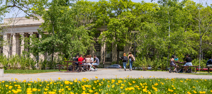 Image of Building 7 and students seated at picnic benches on a sunny Spring day