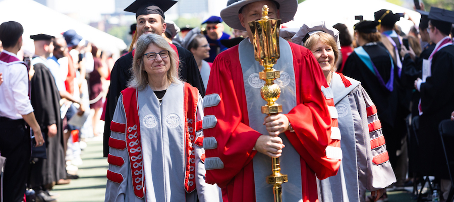 Image of the academic procession being led by Stephen Baker carrying the ceremonial mace, followed by Sally Kornbluth in her presidential regalia