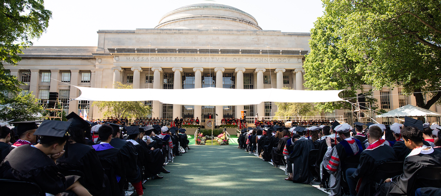 Image looking towards the Commencement stage on Killian Court. Graduates dressed in cap and gown are seated in the audience.