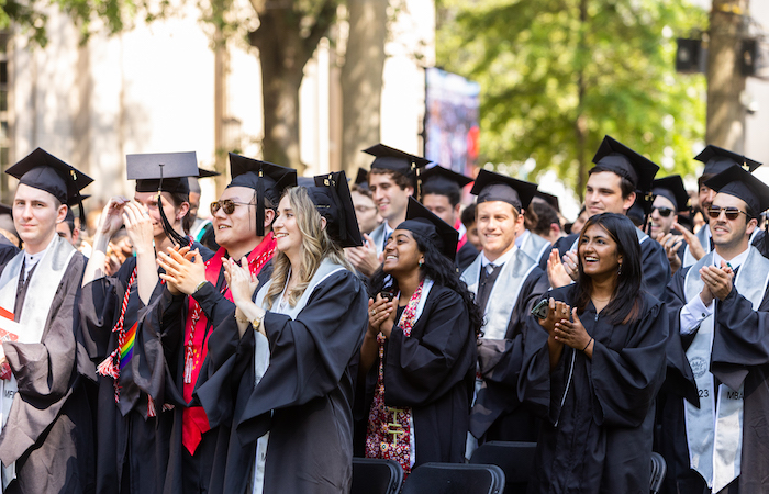 Image of graduates standing and clapping while looking towards the Killian Court stage