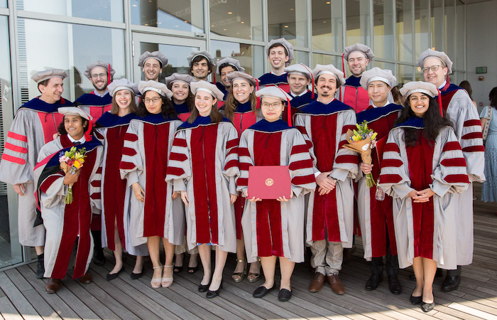 Image of a group advanced degree recipients smiling at the camera