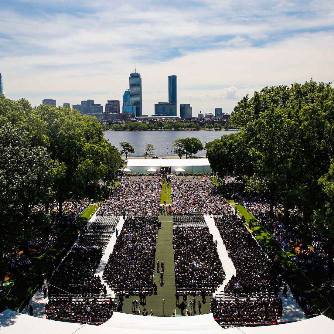 Image of the audience in Killian Court during Commencement, in the foreground, you see the audience, and in the back you see the Charles River and the Boston skyline