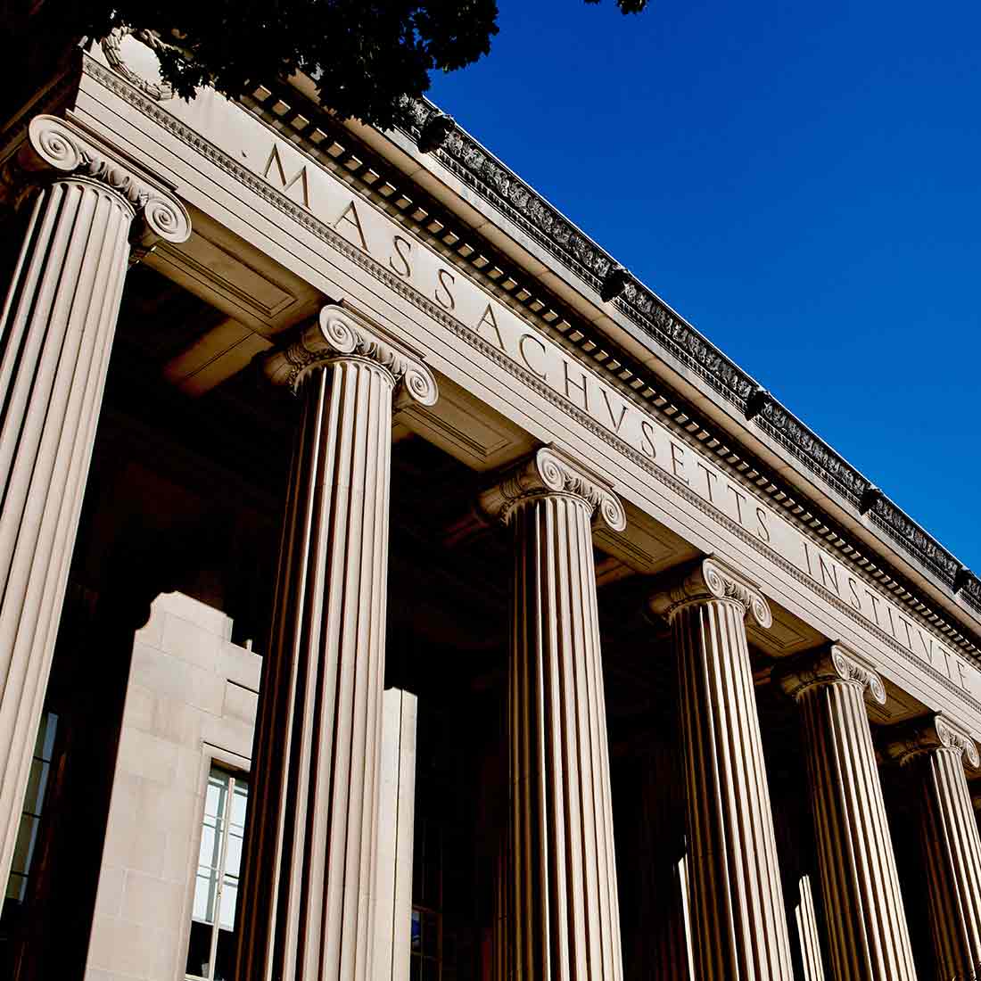 Image of the front columns of MIT’s Lobby 10 under bright blue sky, showing the engraved words ‘Massachusetts Institute of Technology’ across the building’s façade.