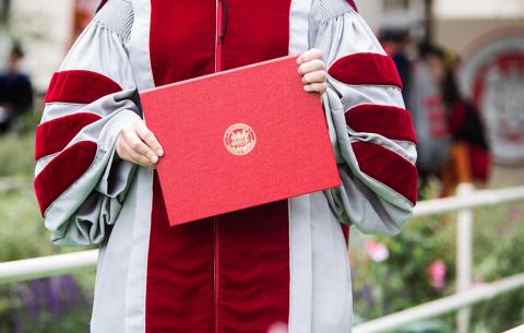 A close shot of a graduate holding the red diploma case while exiting the stage; photo: Jake Belcher