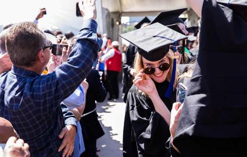 Female graduate poses for the camera while in procession, tilting her sunglasses