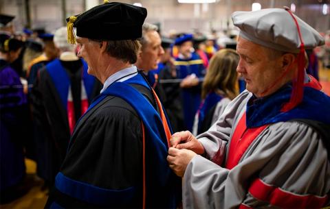 Faculty help one another with their robes and hoods