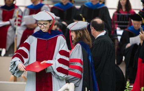 A new PhD graduate holds her diploma as she is greeted by Chancellor Barnhart; photo: Jake Belcher