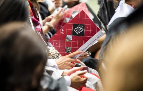 Image of an audience member holding the program for the OneMIT Commencement Ceremony holding a program