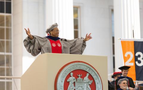 Image of Chancellor Melissa Nobles speaking at the podium, she is smiling and both her hands are raised