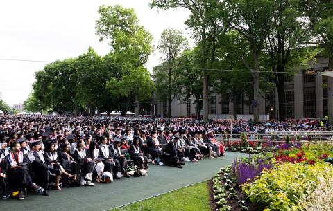 Image of the graduates in the audience standing and looking towards the Commencement stage